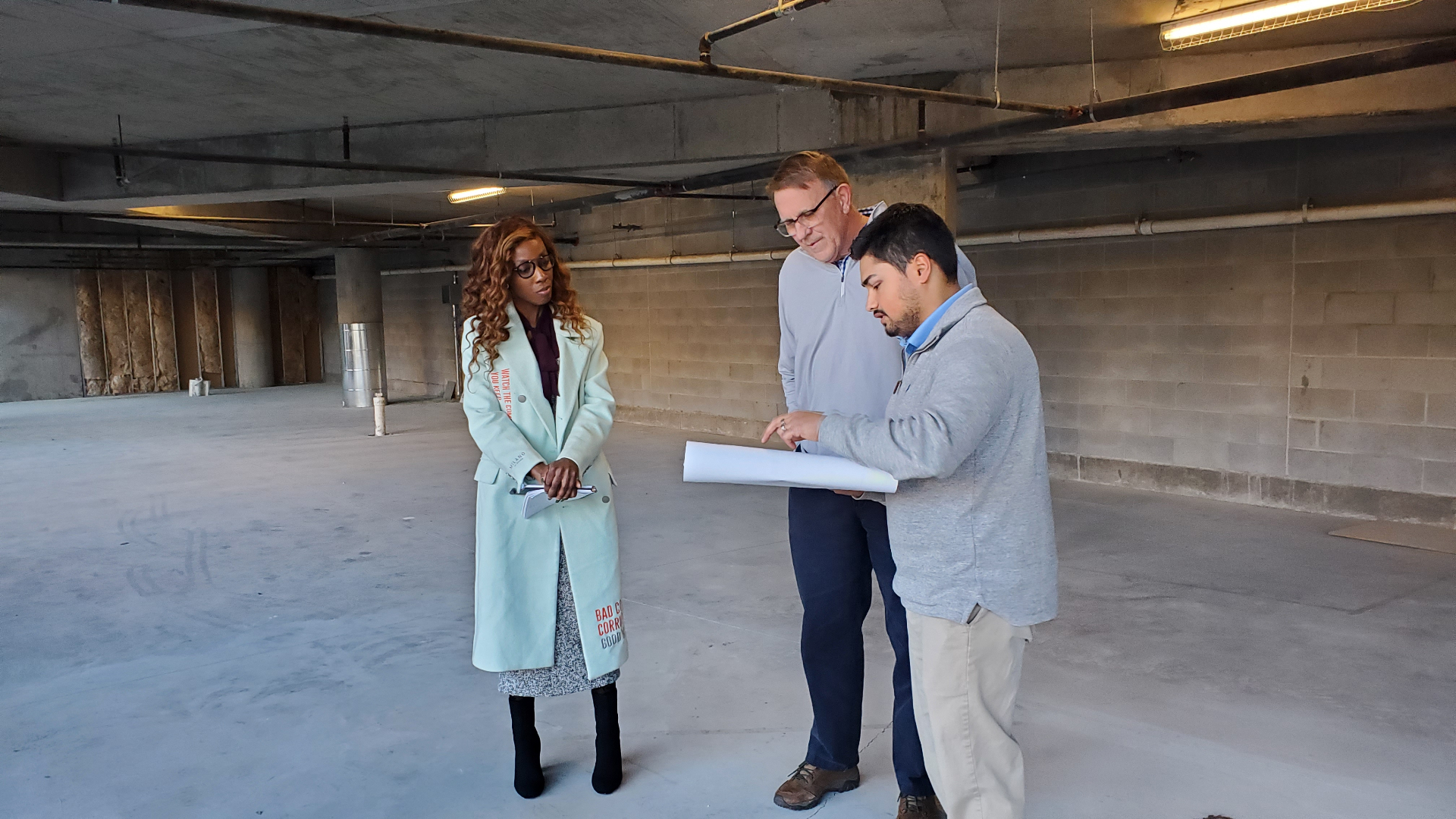 Monique O. Ositelu, PhD on a client site walk with architects, reviewing plans in a raw commercial shell